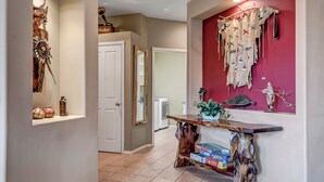 A hallway with a wooden console table, a red accent wall with tribal art, and a door leading to another room. - Experience luxury at Sedona Garden Oasis at Bell Rock, perfect for families! (Sedona)