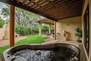 Un jacuzzi bajo una pérgola de madera con zona de patio, mobiliario exterior y vistas a un jardín.