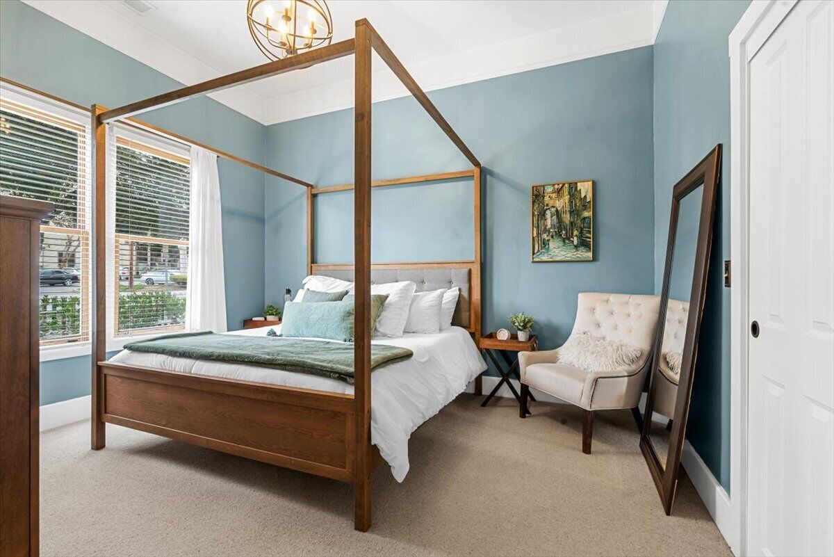 A bedroom with a four-poster bed, a chair, a painting, and a mirror.