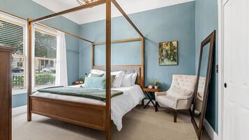 A bedroom with a four-poster bed, a chair, a painting, and a mirror.