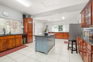 A spacious kitchen with wooden cabinets, a central island, and a large window providing natural light. - Forever Summer Gorgeous 4BDR Villa (Runaway Bay)