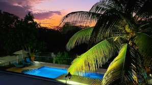 A swimming pool with lounge chairs and umbrellas, surrounded by palm trees and a sunset view. - Forever Summer Gorgeous 4BDR Villa (Runaway Bay)