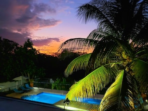 A swimming pool with lounge chairs and umbrellas, surrounded by palm trees and a sunset view. - Forever Summer Gorgeous 4BDR Villa (Runaway Bay)