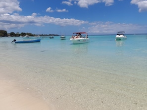 Ein Strand mit klarem türkisblauem Wasser, Booten und einem sandigen Ufer.