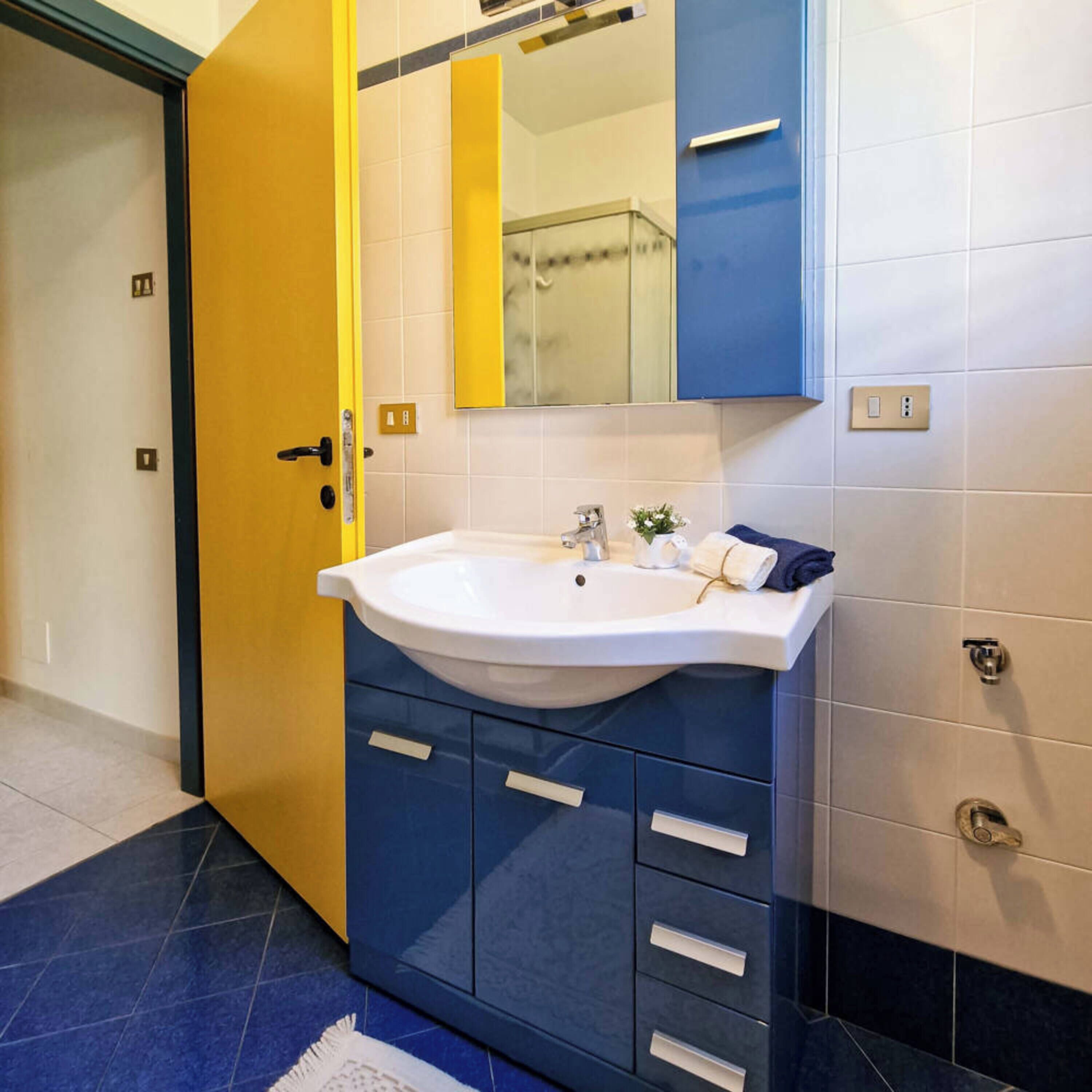 Een badkamer met een wit wastafel, blauwe kastjes en een gele deur.