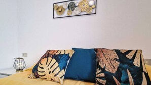 Ein Bett mit gemustertem Überwurf, zwei Kissen mit Blättermotiv und ein dekoratives Wandelement.