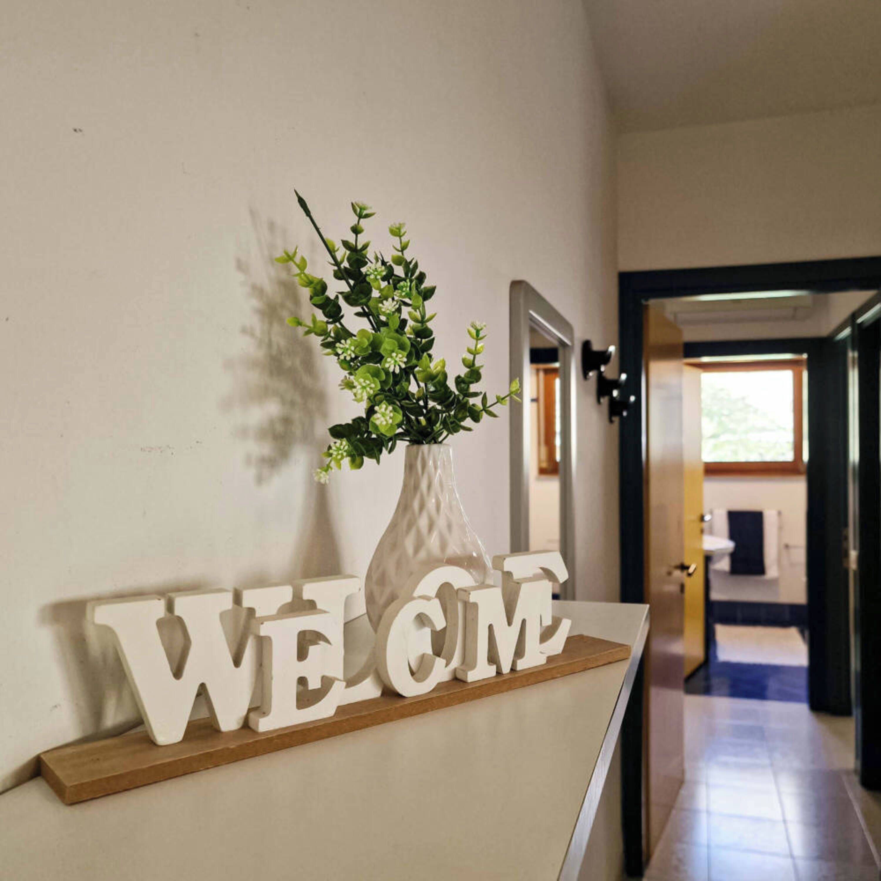 A reception area with a 'WELCOME' sign and a vase with green foliage.