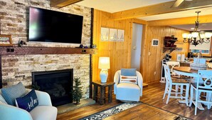Ein gemütliches Wohnzimmer mit Kamin, Fernseher und Essbereich mit Holzmöbeln.