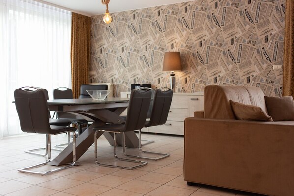 A modern living room with a dining area, featuring a patterned wallpaper, a sofa, a coffee table, and a lamp.