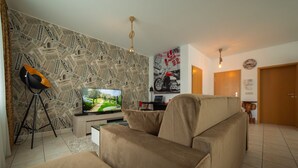 Una sala de estar con televisor, un sofá, un papel tapiz estampado y un cartel de motocicleta.