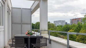 Un balcón con una mesa y dos sillas, con vistas a un paisaje urbano con edificios y árboles.