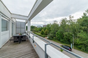 Un balcón con mesa y sillas, con vista a una calle y vegetación.