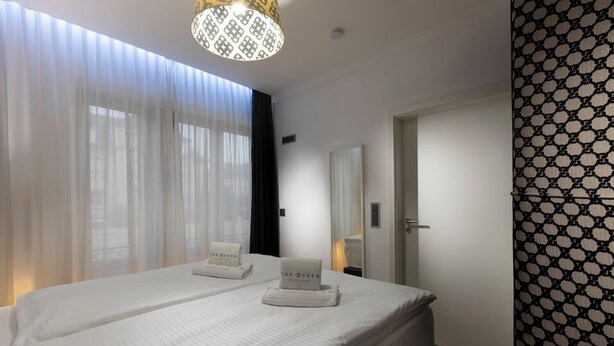 A hotel room with two beds, a large window with sheer curtains, a chandelier, a mirror, and a patterned wall.