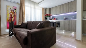 A modern living room with a brown sofa, a painting on the wall, and a kitchen area with a countertop and sink.