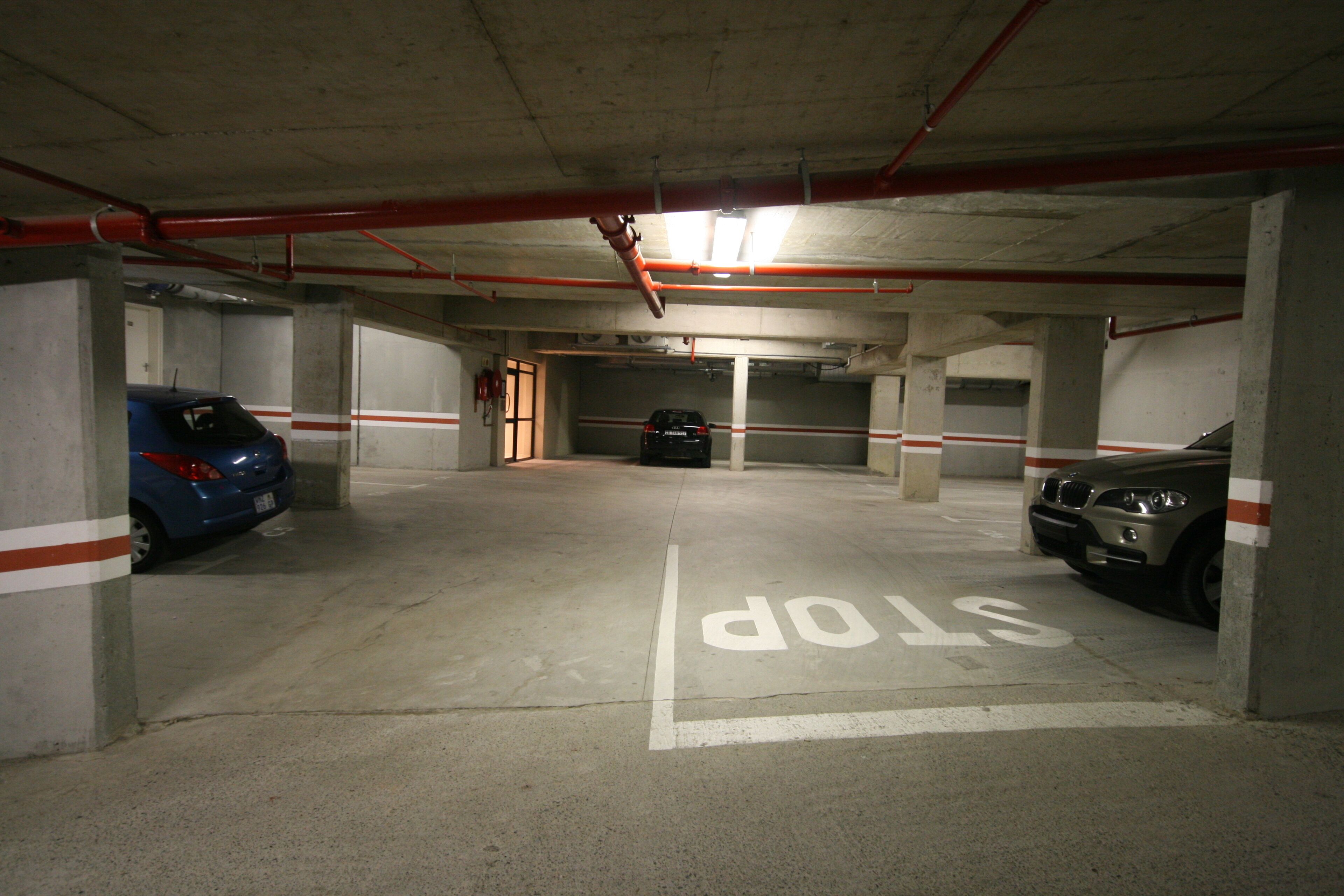 Un parcheggio sotterraneo con pilastri in cemento, posti auto delimitati e un segnale 'STOP' sul pavimento.