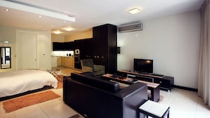 A modern hotel room with a bed, a sofa, a TV, and a kitchen area. - Cosy Studio in Camps Bay (Cape Town)