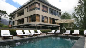 A pool area with lounge chairs and a building with large windows and balconies. - Cosy Studio in Camps Bay (Cape Town)