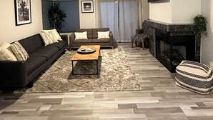 A living room with a dark sofa, a wooden coffee table, a patterned ottoman, a fireplace, and a ceiling fan. - Enjoy a stylish experience at a centrally-located place. Pictures upon request. (Palm Springs)