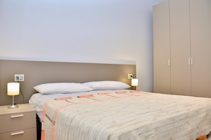 A bedroom with a bed, bedside lamps, a nightstand, and a wardrobe.