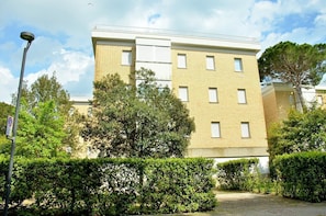 Um edifício residencial de vários andares com fachada de tijolos, diversas janelas e um acesso pavimentado.