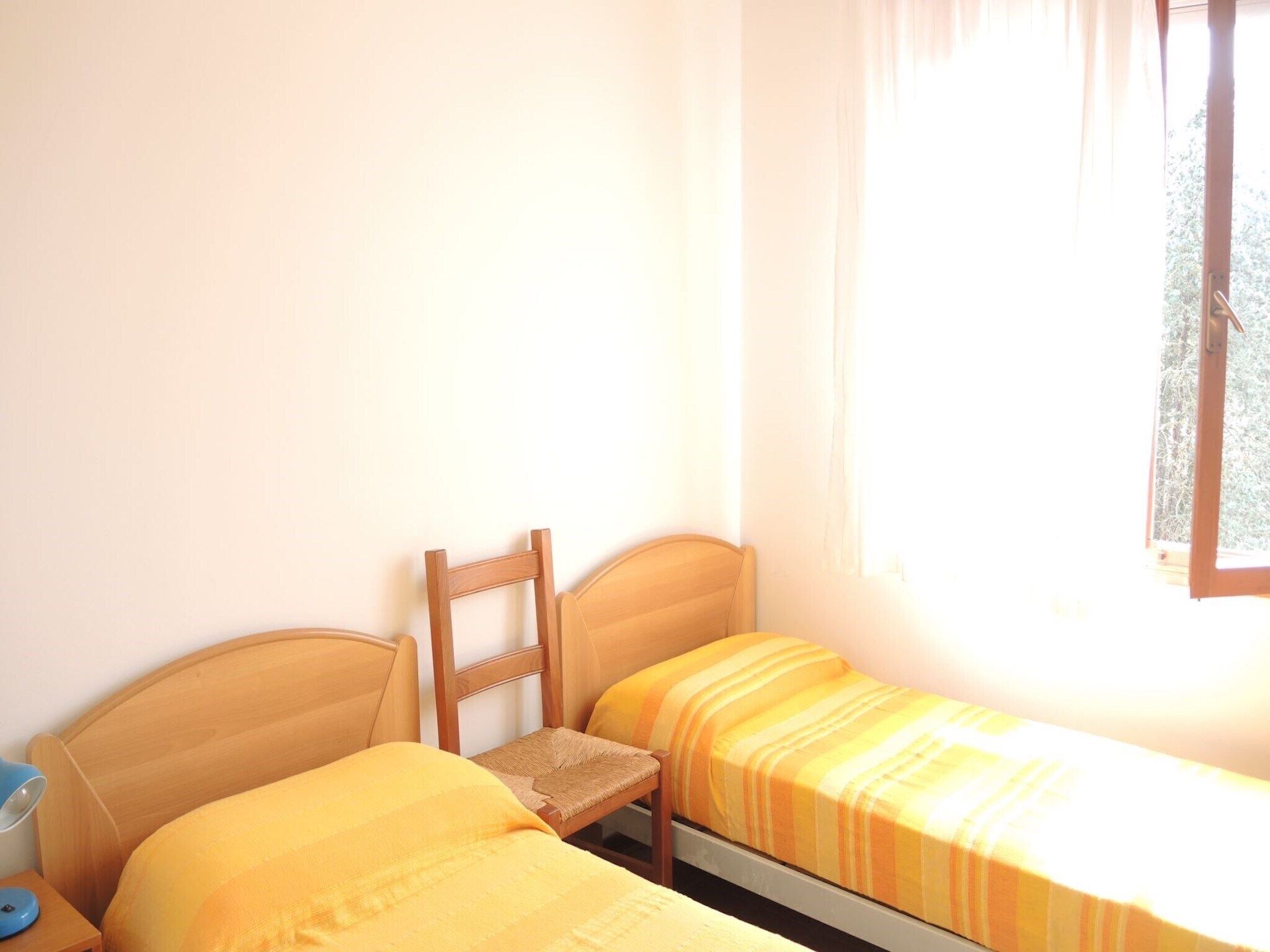 A small room with two beds, a chair, and a window with curtains.