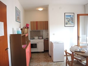 Cocina compacta equipada con refrigerador, horno y microondas. Cuenta con una mesa de comedor con sillas y una ventana con vistas.