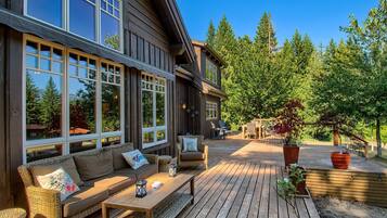 Une terrasse en bois avec des sièges d’extérieur, de grandes fenêtres et une vue sur les arbres.