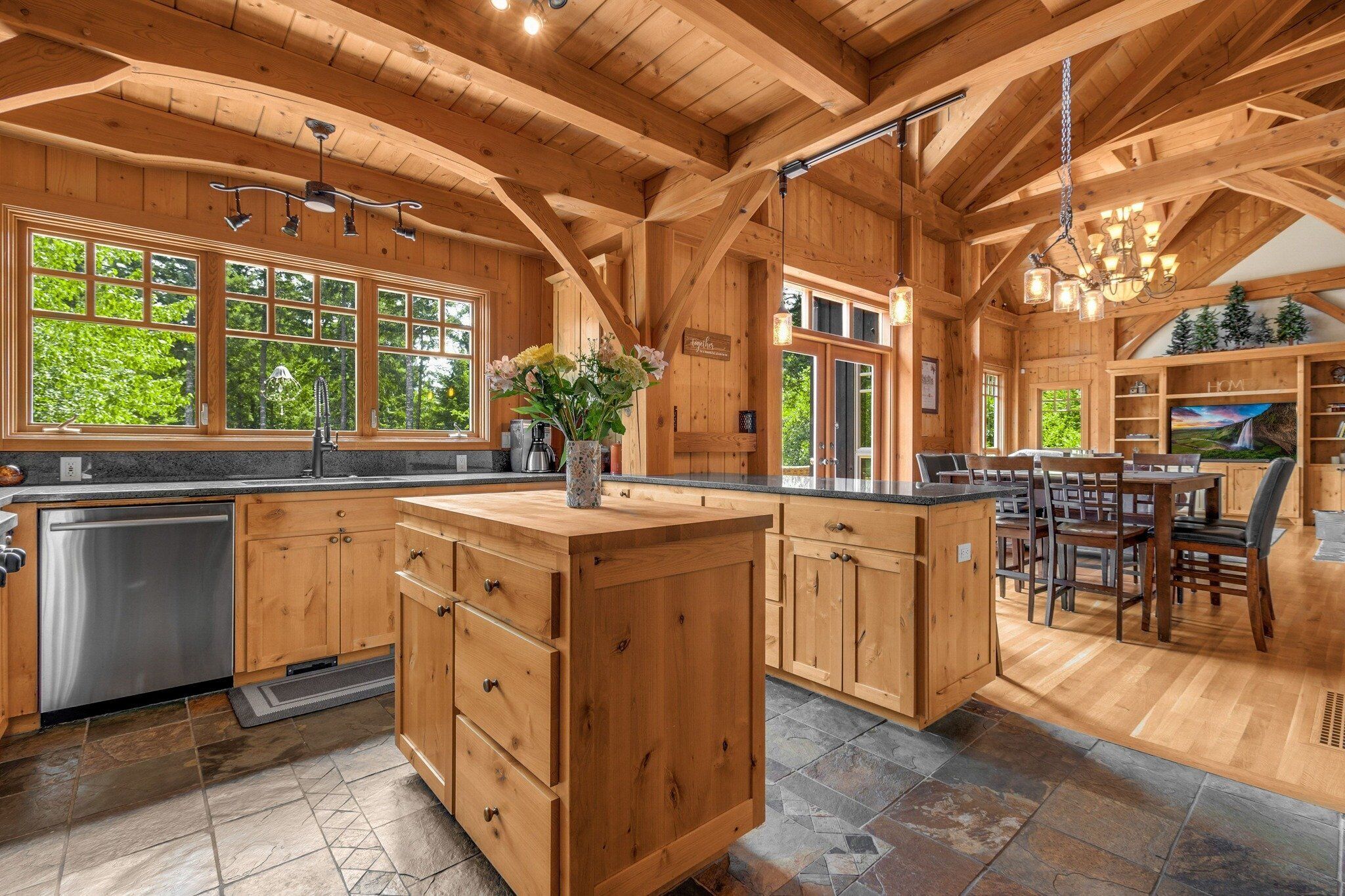 Une cuisine spacieuse dotée de meubles en bois, d’un îlot central et de grandes fenêtres offrant une vue sur la verdure.