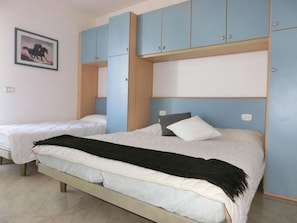 A bedroom with two beds, one larger and one smaller, with a blue wardrobe above the larger bed.