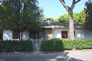 A single-story house with a white exterior, a front door, and a small porch. - Comfortable Villa in a Quiet Spot in Bibione (San Michele al Tagliamento)