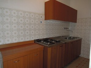 A kitchen with a gas stove, sink, wooden cabinets, and patterned wall tiles. - Comfortable Villa in a Quiet Spot in Bibione (San Michele al Tagliamento)