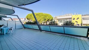 Un balcón con suelo de baldosas, una mesa con sillas y vistas a edificios y árboles.