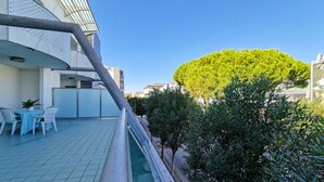 Una terraza en la azotea con piscina, sillas blancas y un árbol bien cuidado.