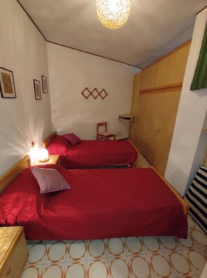 Une petite pièce agréable et chaleureuse, avec deux lits, une armoire en bois, une chaise et une petite table.