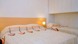 A hotel room with two beds, a nightstand, and a wall-mounted lamp. - Relaxing Flat With Balcony in Bibione Pineda (San Michele al Tagliamento)