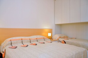A hotel room with two beds, each with a headboard and a bedside lamp. - Relaxing Flat With Balcony in Bibione Pineda (San Michele al Tagliamento)