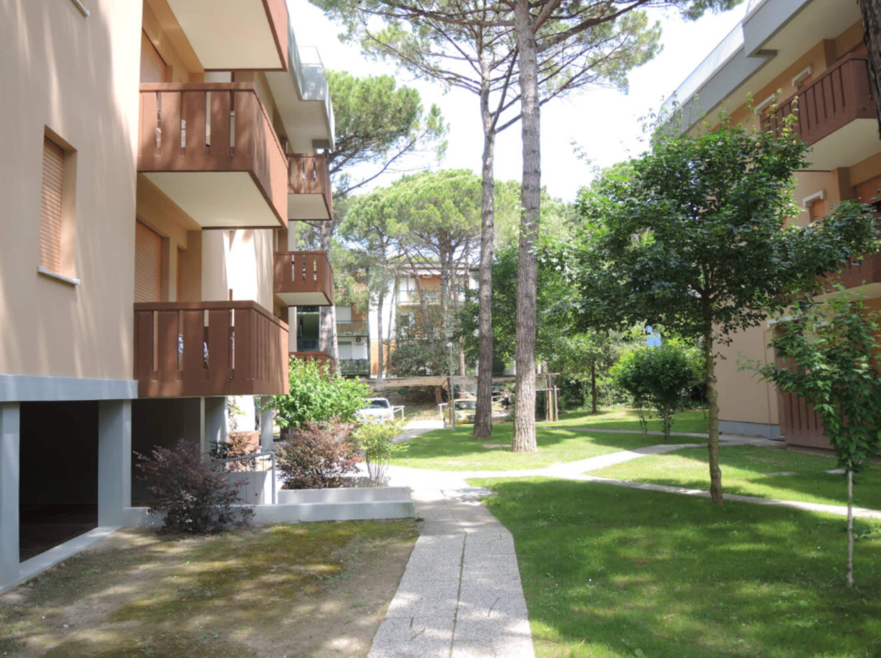 A courtyard with a pathway, trees, and a building with balconies.