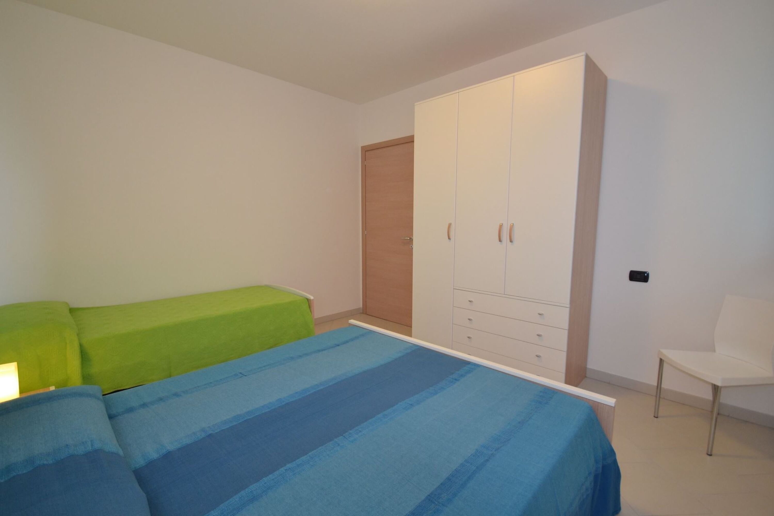Un dormitorio con una cama, un sofá verde, una silla blanca y un armario.