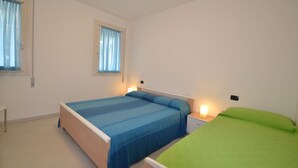 A bedroom with two beds, a bedside table, and a window with curtains. - Modern Flat With Private Garden (Rosolina)