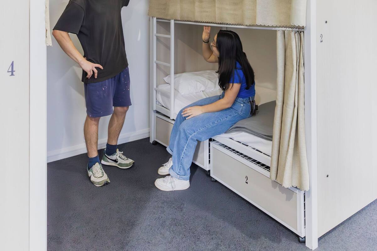 A bunk bed with a person standing and another sitting.