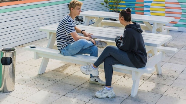 Dos personas sentadas en una mesa blanca al aire libre, con una vista panorámica de la ciudad al fondo.