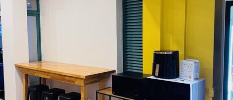 A compact kitchen with a wooden table, black stools, and a black and white microwave on a metal shelf.