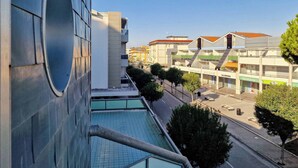 Un edificio moderno con un gran ventanal circular, una terraza en la azotea y vistas a una calle con otros edificios y árboles.