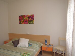 A hotel room with a bed, a nightstand, a chair, a painting on the wall, and a window with curtains. - Nice Flat for 6 Guests With Private Garden (San Michele al Tagliamento)