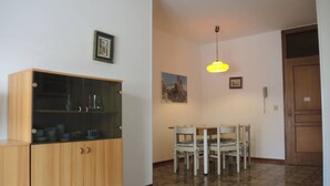 Un coin repas comprenant un buffet en bois, une table avec des chaises, un luminaire suspendu et une porte.