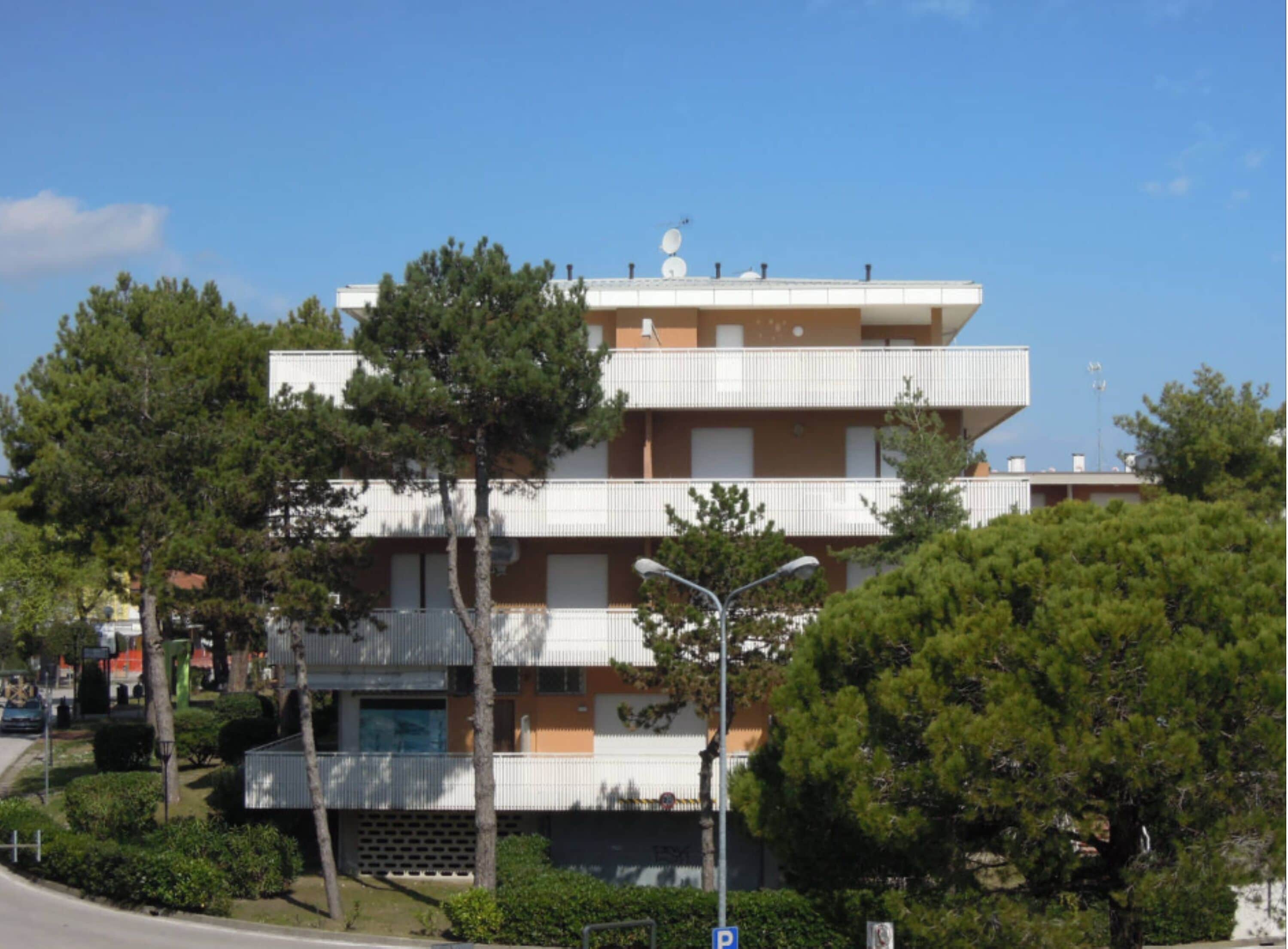 A multi-story building with balconies, surrounded by trees and a clear sky.