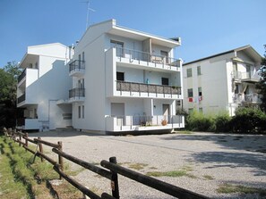A multi-story building with balconies, a gravel driveway, and a wooden fence.