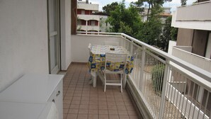 Un balcon avec un sol carrelé, une table recouverte d’une nappe à motifs et une chaise.