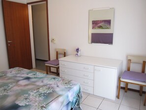 A bedroom with a bed, a desk, two chairs, and a small vase with flowers.