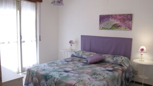 Une chambre à coucher avec un lit, une table de chevet, une lampe, un tableau et une fenêtre avec des rideaux.